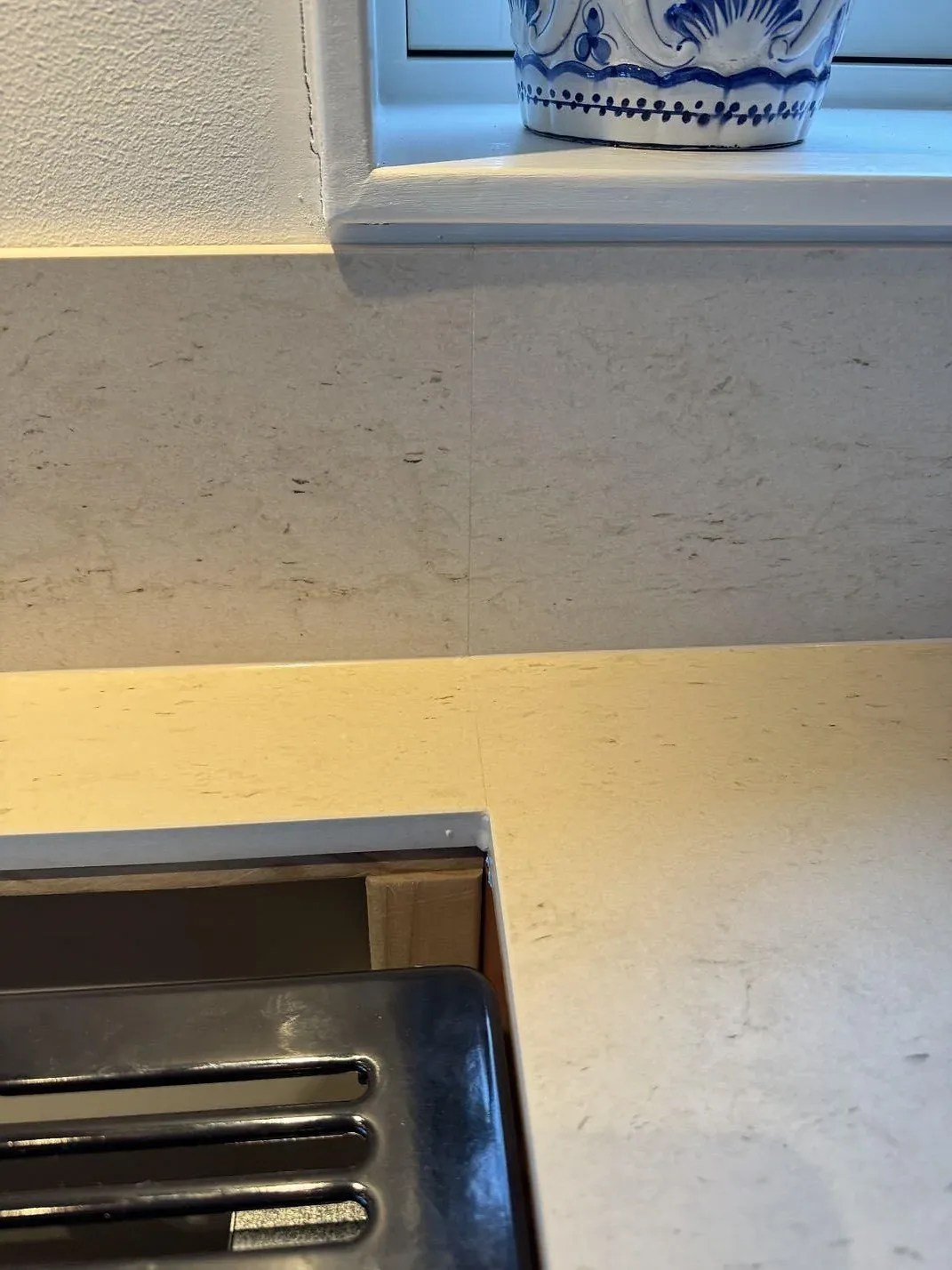 Närbild på matt Dekton Danae keramik vid hällkant och uppvikt stänkskydd under fönster i Hakenäset.