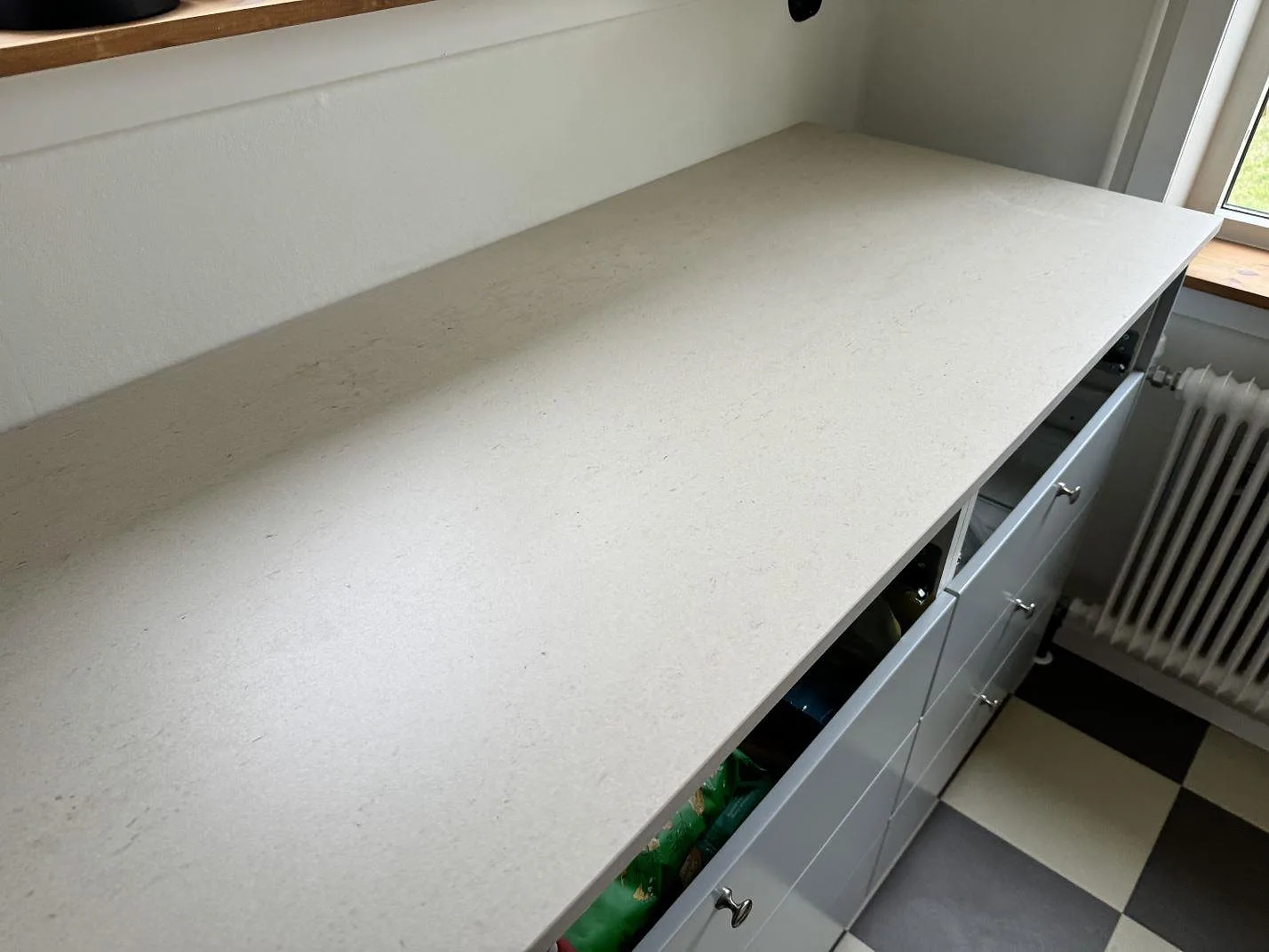 Närbild av den långa köksbänken i matt Dekton Danae med ljus yta och rutigt golv i Höör.