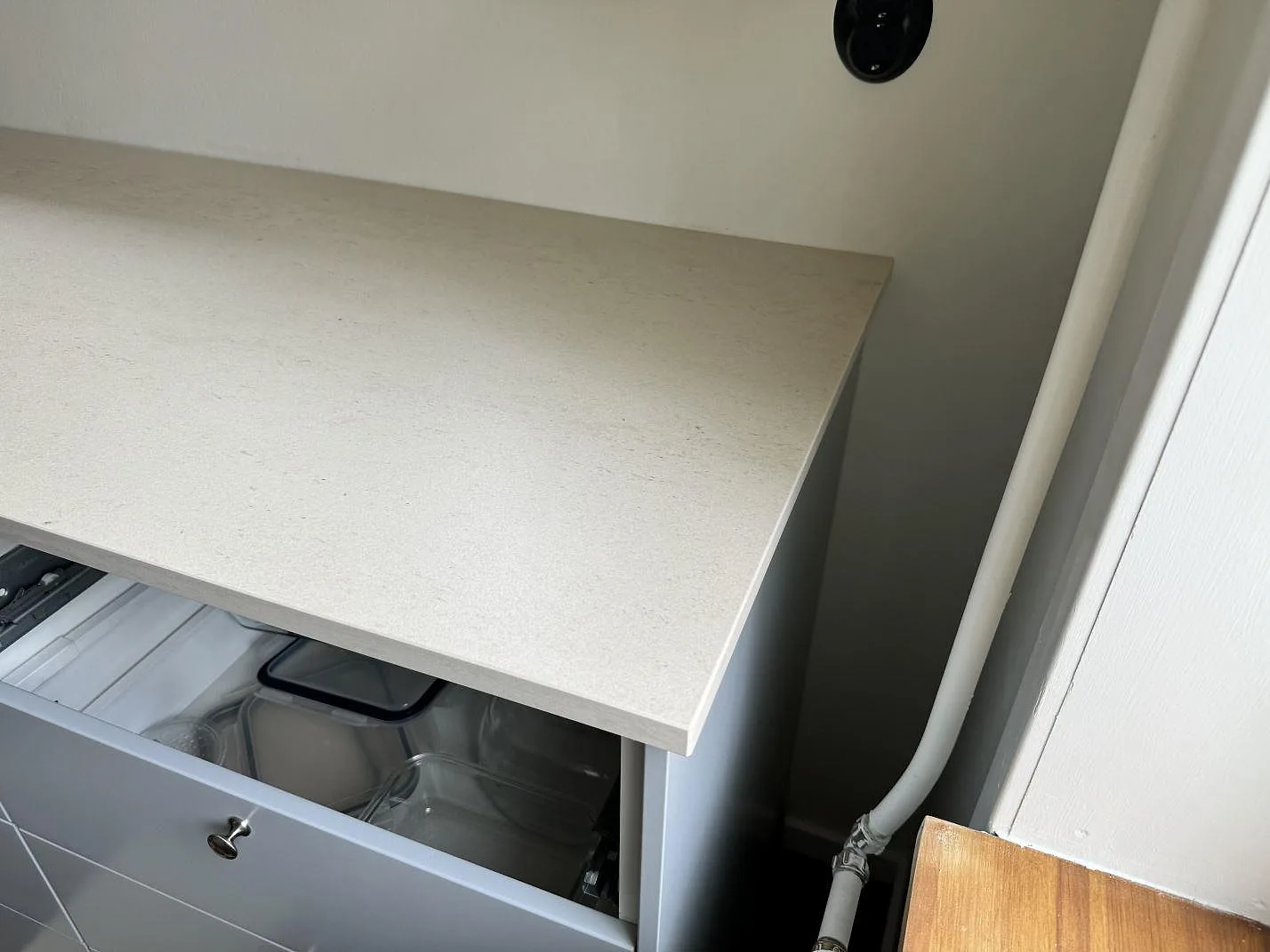 Detalj av avslut och framkant på matt Dekton Danae ovanför ljusa kökslådor i Höör.