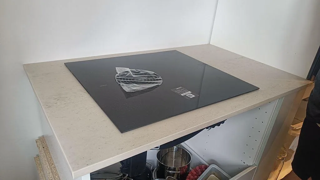 Svart induktionshäll på matt Dekton Danae köksbänkskiva av ljus keramik, med öppna köksstommar under montering i København N.
