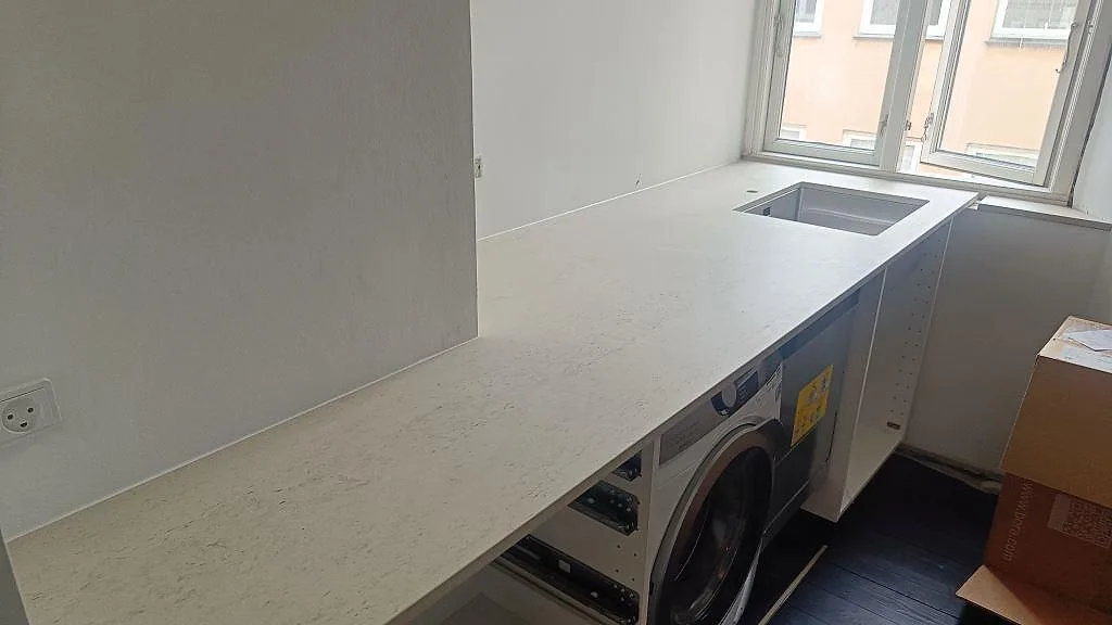 L-formad köksbänkskiva i matt Dekton Danae keramik, 20 mm, med underlimmad rostfri diskho vid fönster i ett kök under montering i København N.