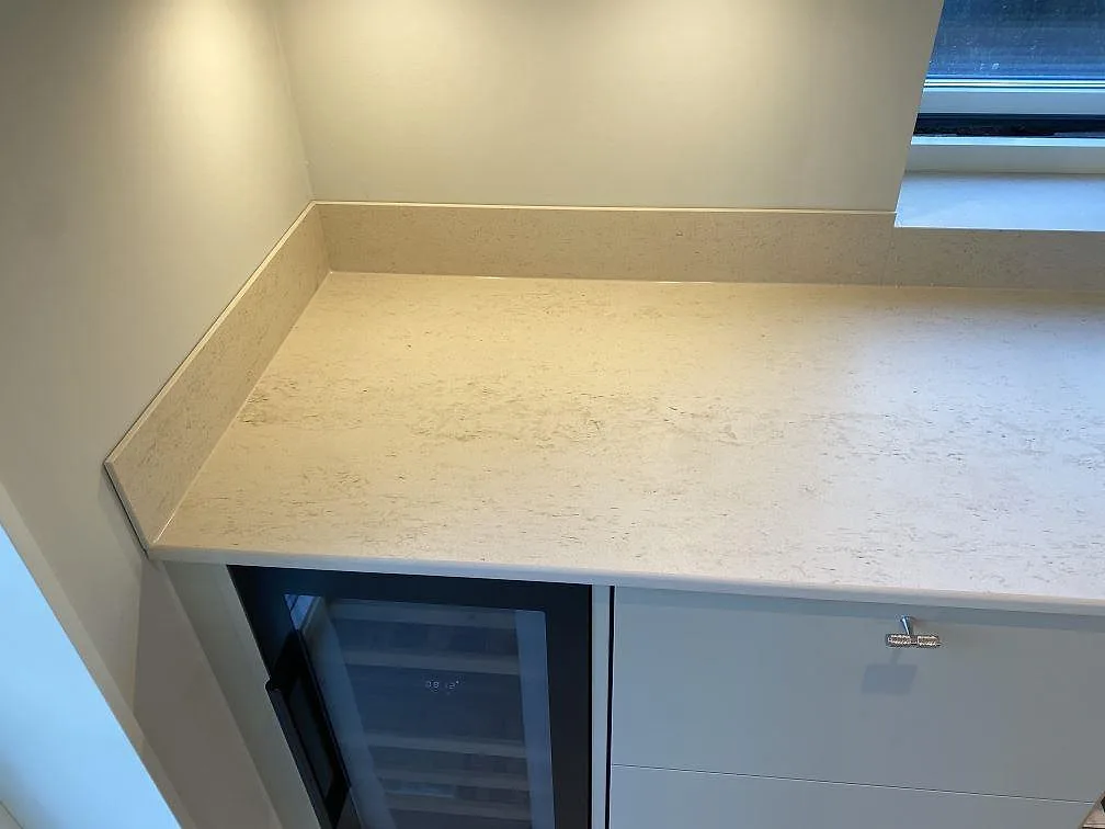 Sidobänk i matt Dekton Danae keramik med stänkkant, fönsternisch och ljusa köksluckor i Lerum.