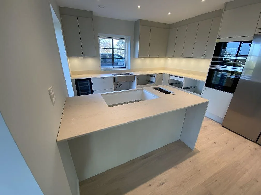 Köksbänkskiva i Dekton Danae, matt gråbeige keramik, i ett U-format kök med köksö och uppvikt stänkkant i Lerum.