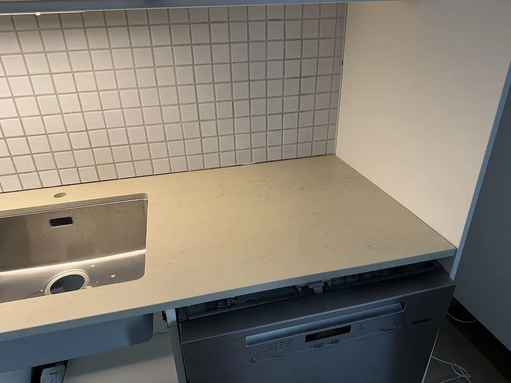 Köksbänkskiva i matt Dekton Danae vid diskdelen, med ljus keramikyta mot kakel i Limhamn.