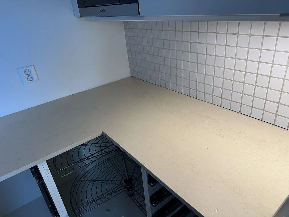Hörnparti med köksbänkskiva i matt Dekton Danae, ljus keramikyta mot kakel och öppna stommar i Limhamn.