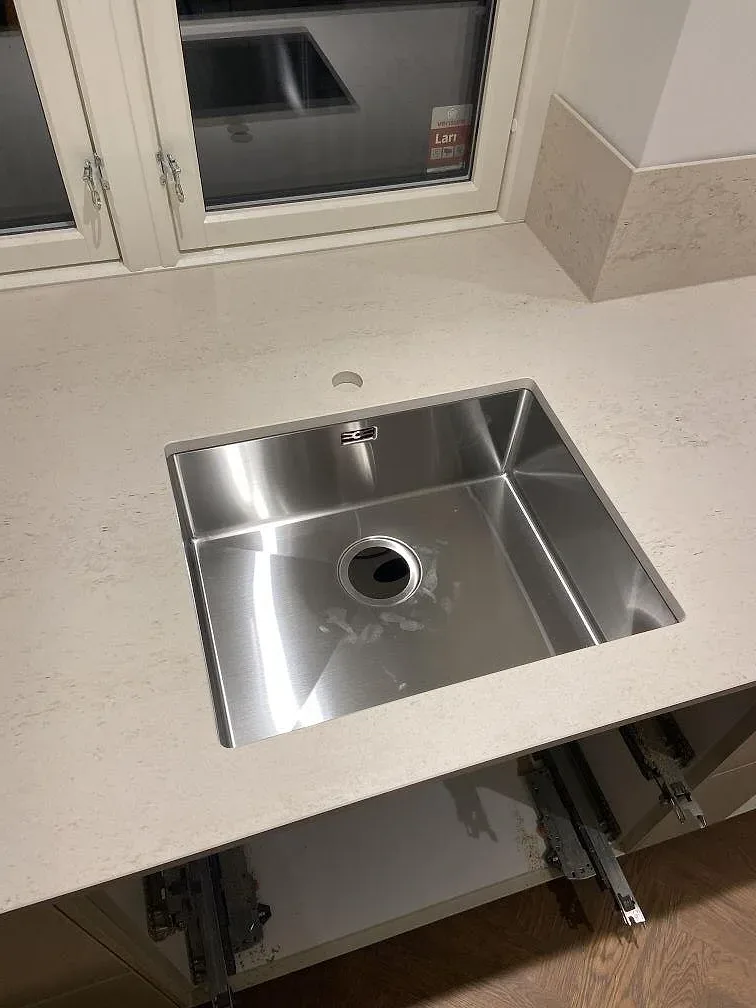 Närbild på underlimmad rostfri diskho i matt Dekton Danae bänkskiva i ett kök i Lomma.