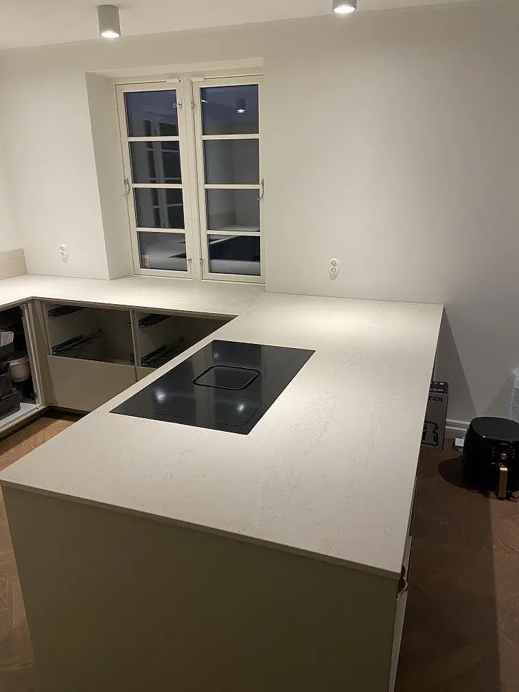 Köksbänkskiva i Dekton Danae, matt taupe ultrakompakt yta, med infälld induktionshäll och fönster i ett kök under montering i Lomma.