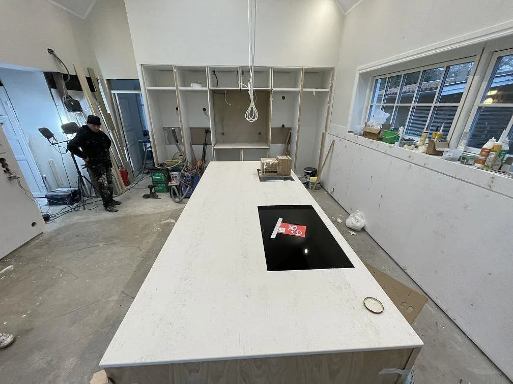 Köksbänkskiva och köksö i ljust greige Dekton Danae, matt, med infälld svart induktionshäll i ett kök under montering i Malmö.