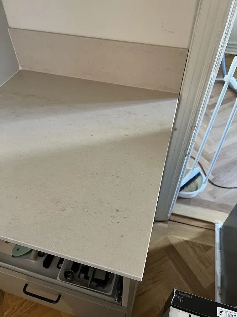 Sidovy av matt Dekton Danae med låg stänkkant och ljusa kökslådor under montering i Malmö.