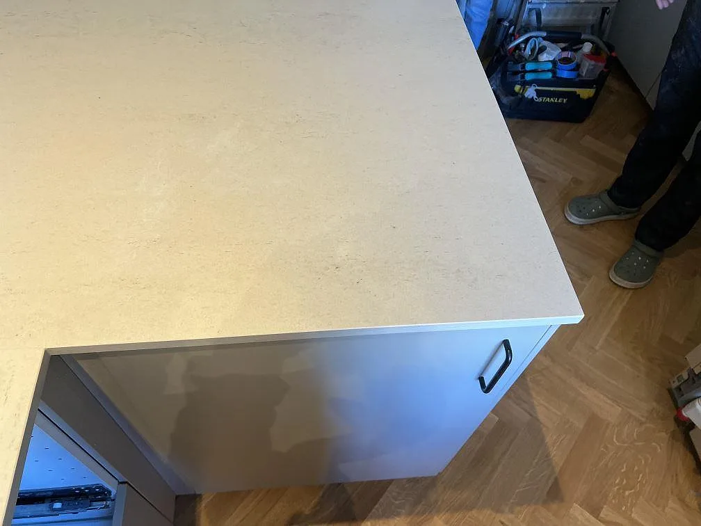 Kantdetalj på köksö i matt Dekton Danae med ljus front, parkettgolv och monteringsmiljö i Malmö.