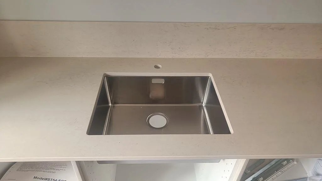 Närbild på underlimmad rostfri diskho i en matt Dekton Danae bänkskiva med ljust stänkskydd i Malmö.