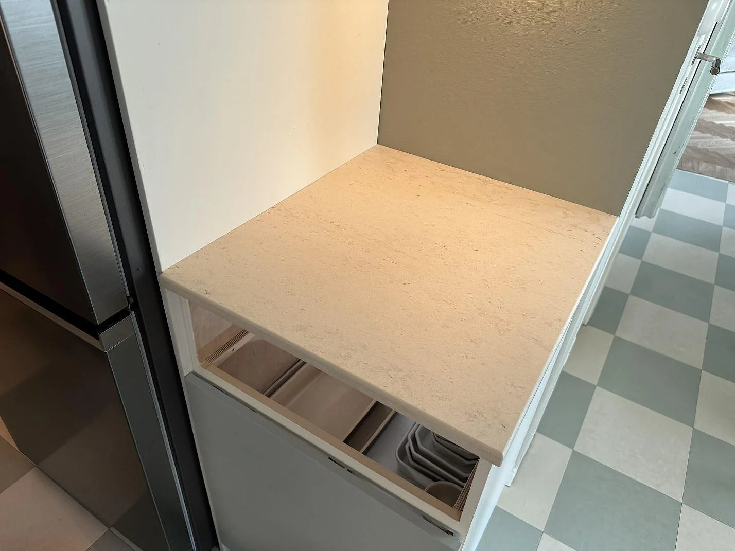Mindre avställningsyta i matt Dekton Danae, keramik, monterad vid kyl och öppna stommar i ett kök i Malmö.