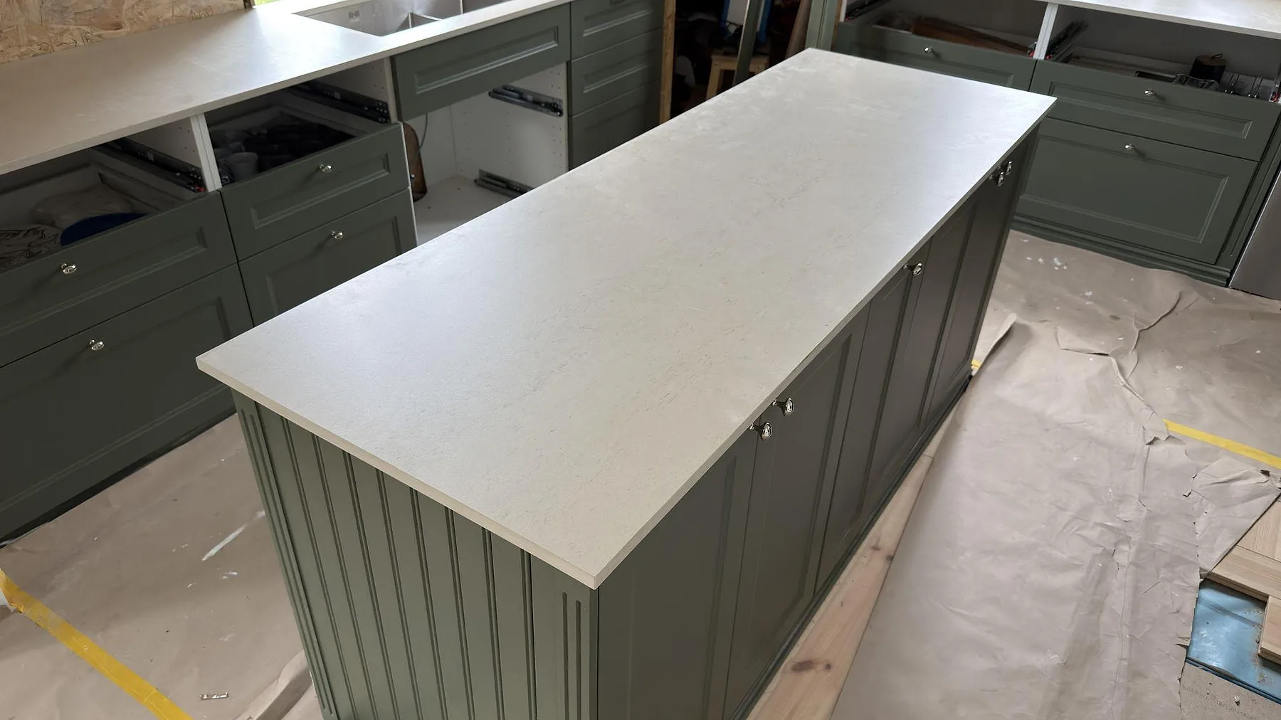 Närbild av köksö med matt Dekton Danae bänkskiva, ljus stenstruktur och gröna stommar i Österbybruk.