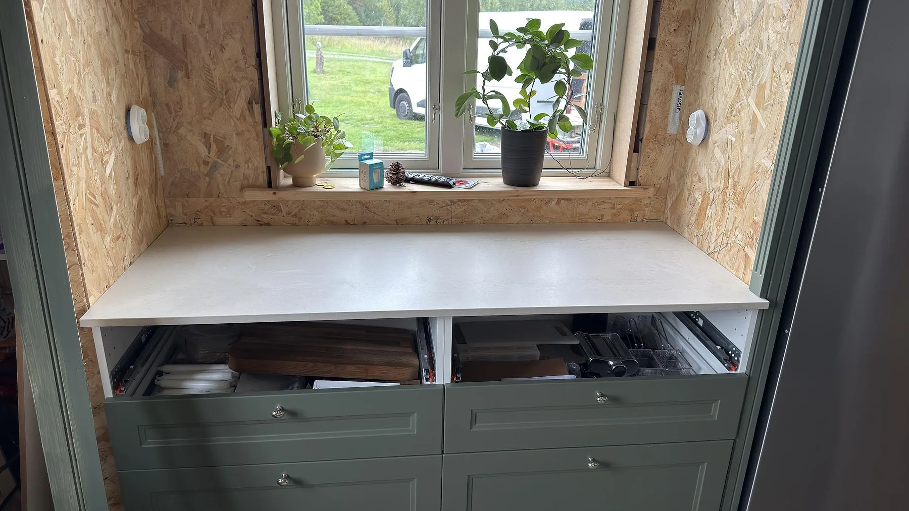 Bänkskiva i matt Dekton Danae under fönster med gröna köksstommar och synlig arbetsyta i Österbybruk.