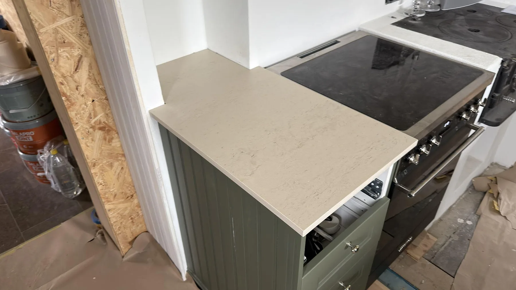 Sidobänk i matt Dekton Danae bredvid spis, med ljus stenstruktur och grön köksstomme i Österbybruk.
