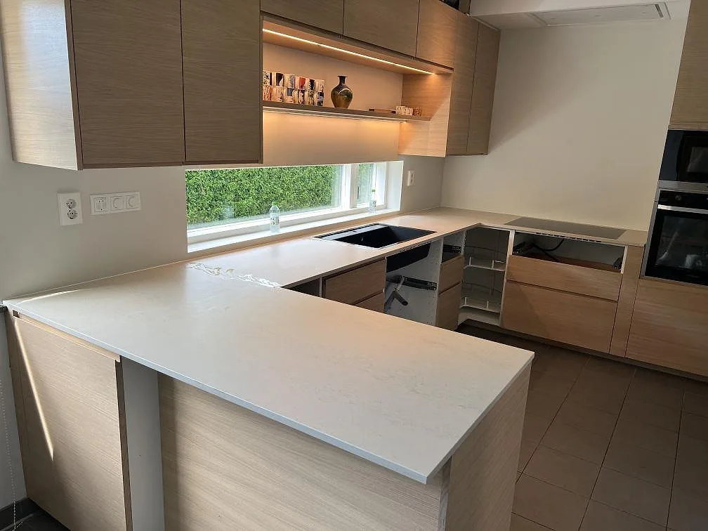 Köksbänkskiva i matt Dekton Danae med halvö, underlimmad svart diskho och svart häll i ett kök med träinredning i Trelleborg.