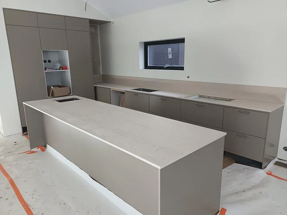 Köksbänkskiva och köksö i Dekton Danae, matt cremevit keramik med diskret ådring, i ett kök i Västerås under montering.