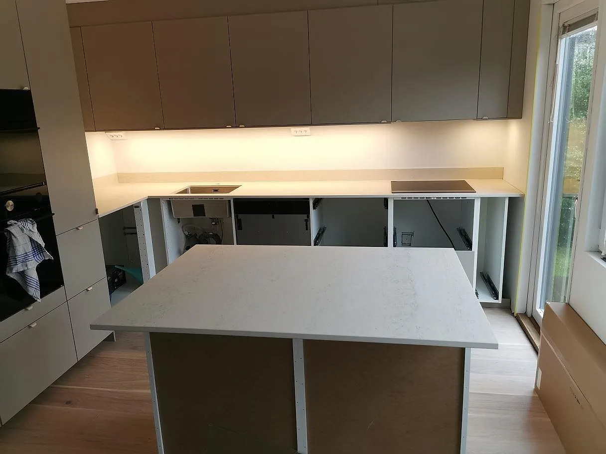 Köksbänkskiva och köksö i Dekton Danae, matt warm greige, under montering i ett kök i Vellinge med induktionshäll och öppna stommar.