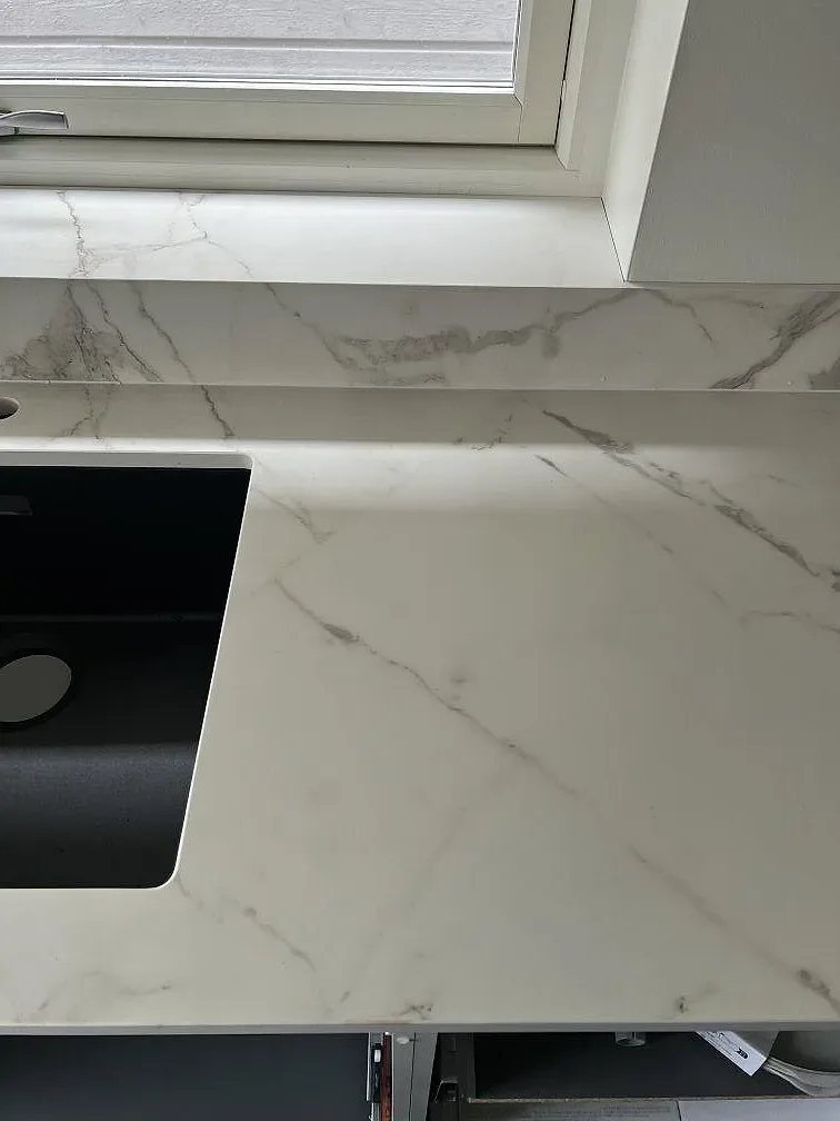 Detalj av matt Dekton Daze KC Velvet runt fönsternisch, stänkkant och svart diskho i ett kök i Malmö.
