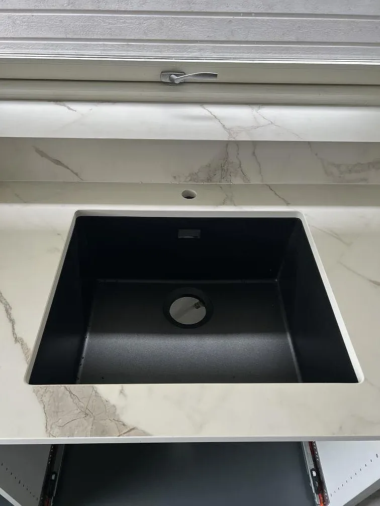 Närbild på svart diskho i en matt Dekton Daze KC Velvet bänkskiva med matchande stänkkant vid fönster i Malmö.
