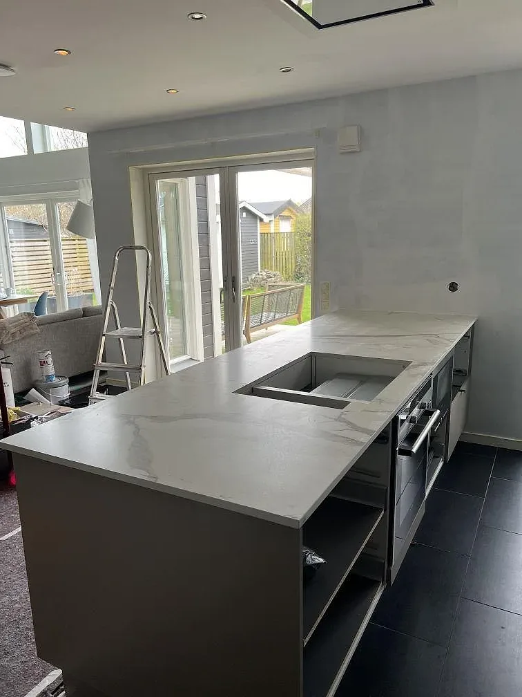 Köksbänkskiva i vit Dekton Daze KC Velvet, matt, med grå ådring och svart diskho i ett kök under montering i Malmö.