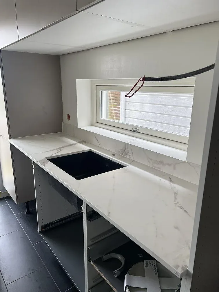 Ljus köksbänkskiva i matt Dekton Daze KC Velvet med låg stänkkant och fönsternisch i Malmö.