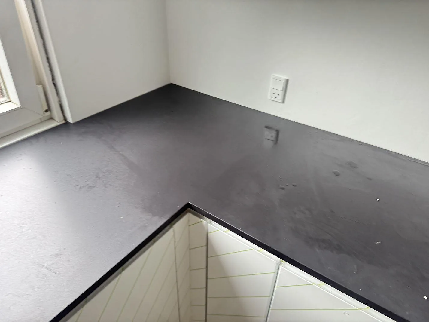 Köksbänkskiva i mörk matt Dekton Domoos, 20 mm, längs ett hörn och fönster i ett kök i Glostrup.