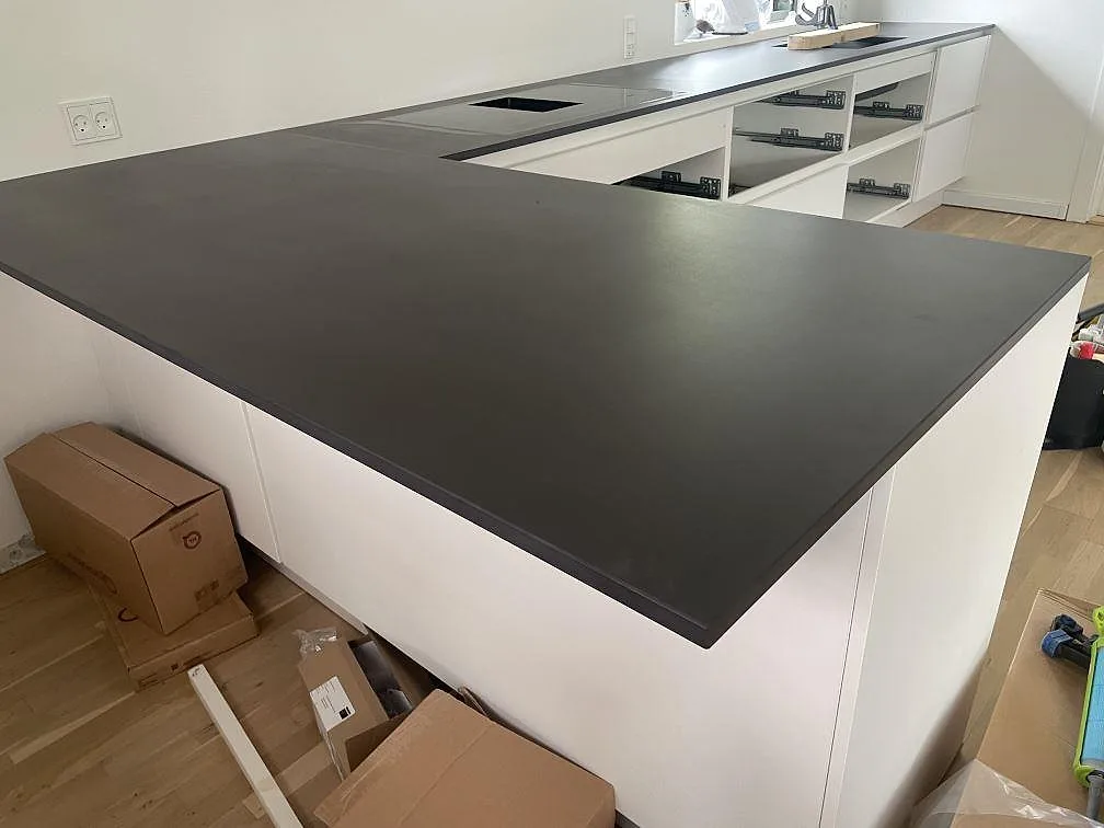 L-formad köksbänkskiva i mörk matt Dekton Domoos keramik med peninsula och hällurtag i ett kök i Greve.
