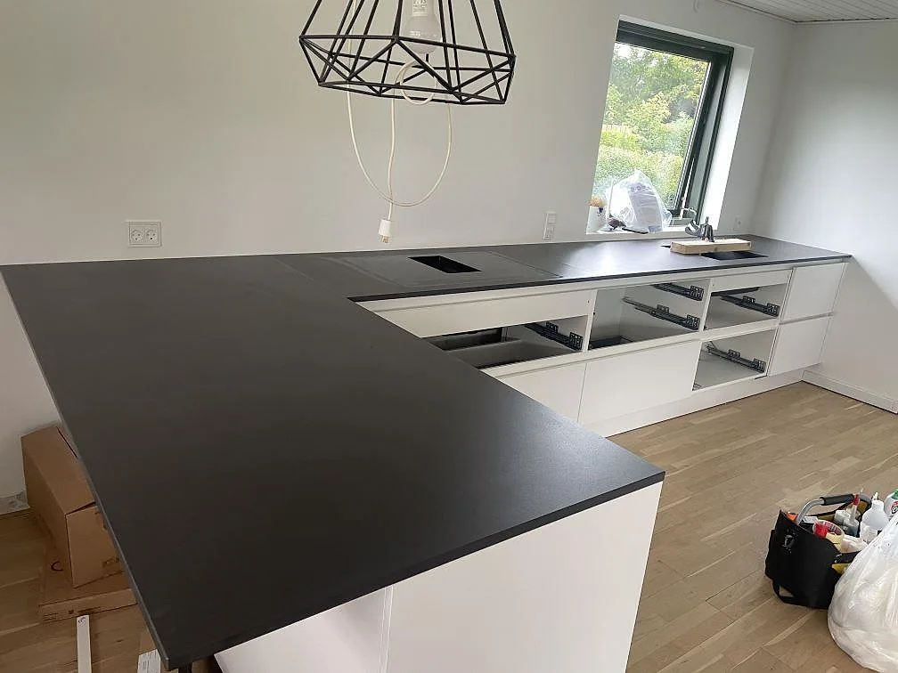 Köksbänkskiva i matt Dekton Domoos keramik med öppen stomme, hällurtag och diskbänk framför stora fönster i Greve.