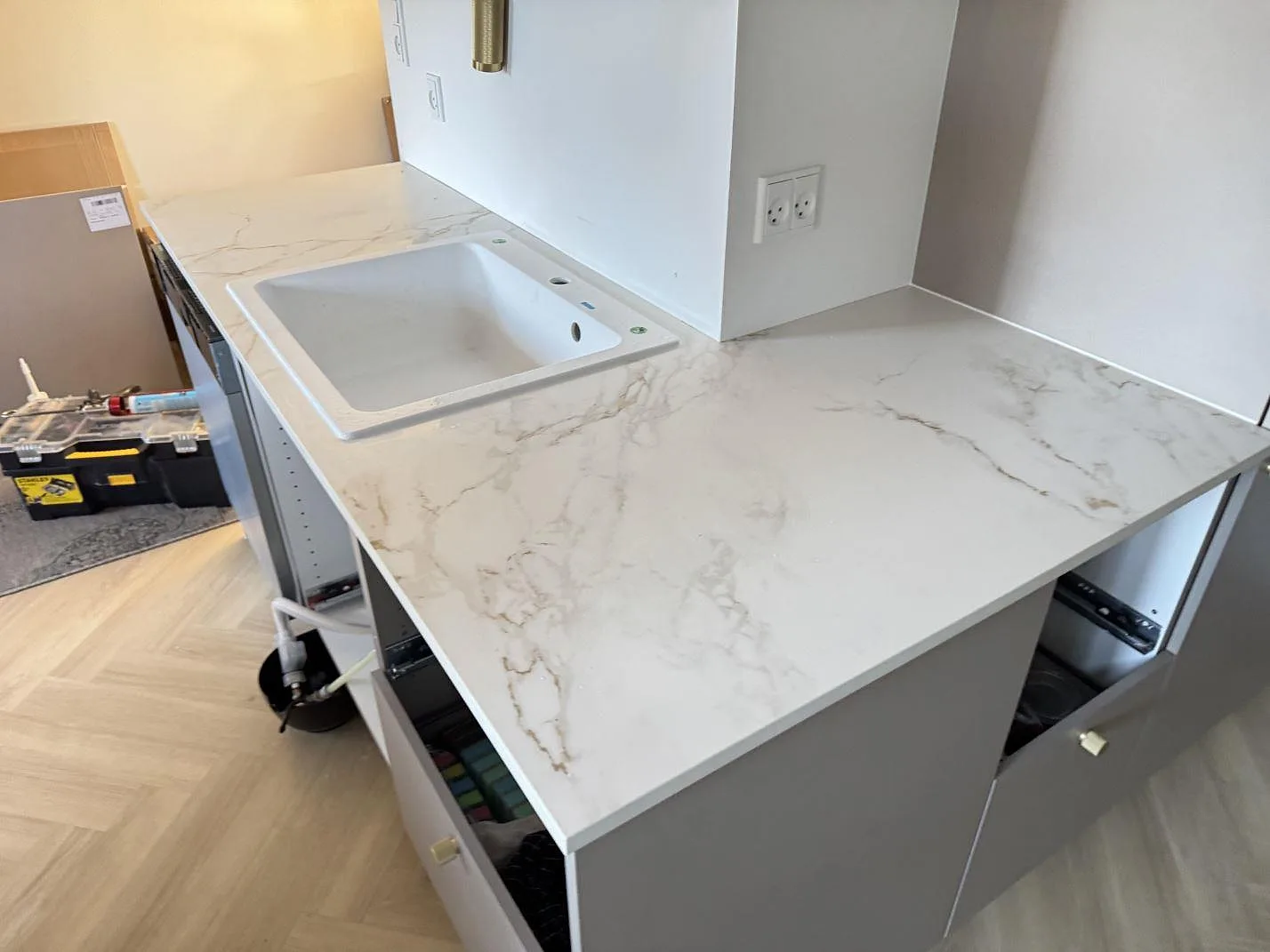 Köksbänkskiva i matt Dekton Entzo, vit keramik med gråbeige ådring, med diskho och arbetsyta under montering i Danmark.