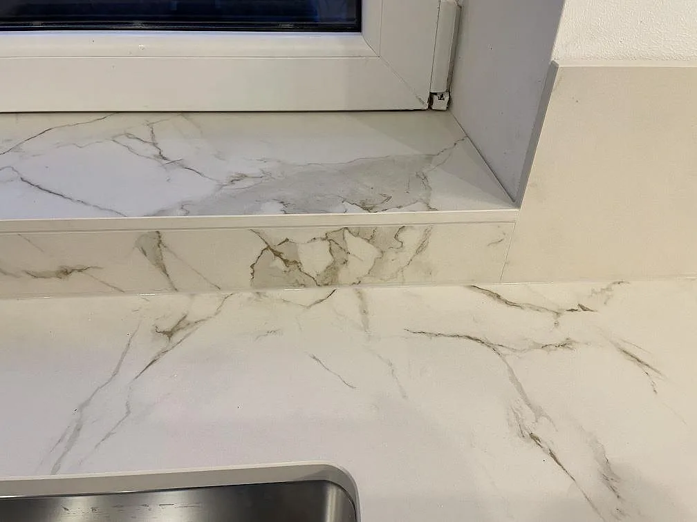Stenklädd fönsterbänk och bänkskiva i matt vit Dekton Entzo keramik med fina grå ådror i ett kök i Ekeby.