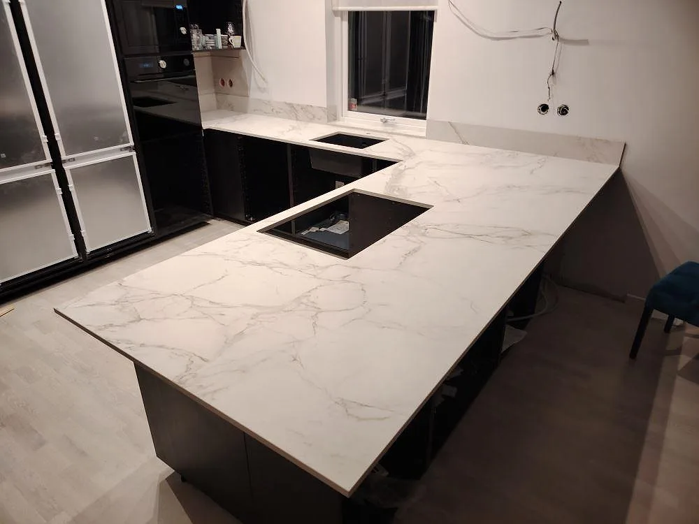 L-formad köksbänkskiva i matt Dekton Entzo keramik med hällplats, diskhozon och lågt stänkskydd i ett kök i Enköping.