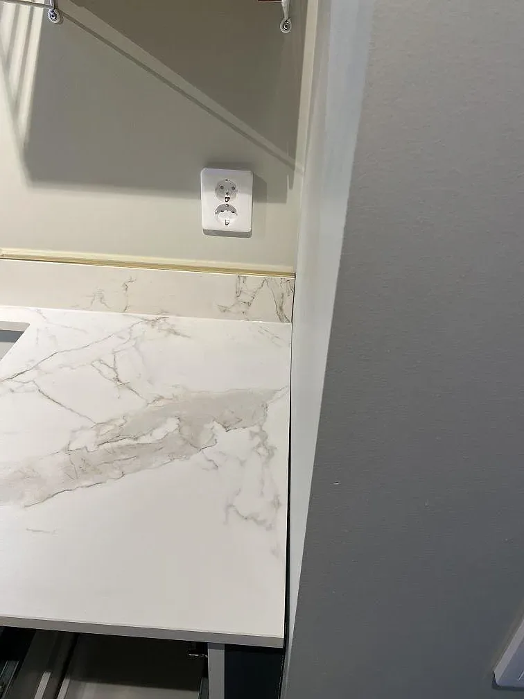 Köksbänkskiva i vit Dekton Entzo med Calacatta-lik ådring och ett lågt uppvikt stänkskydd i ett kök i Falsterbo.