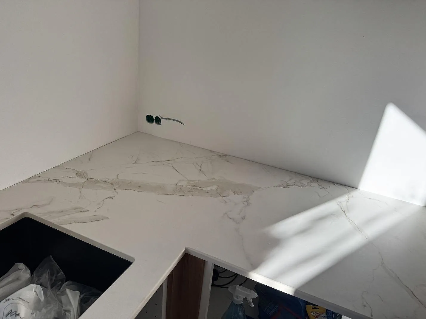 Vinklad köksbänk i Dekton Entzo (Calacatta-look) i keramik med underlimmad svart kompositdiskho i ett kök i Frederikssund.