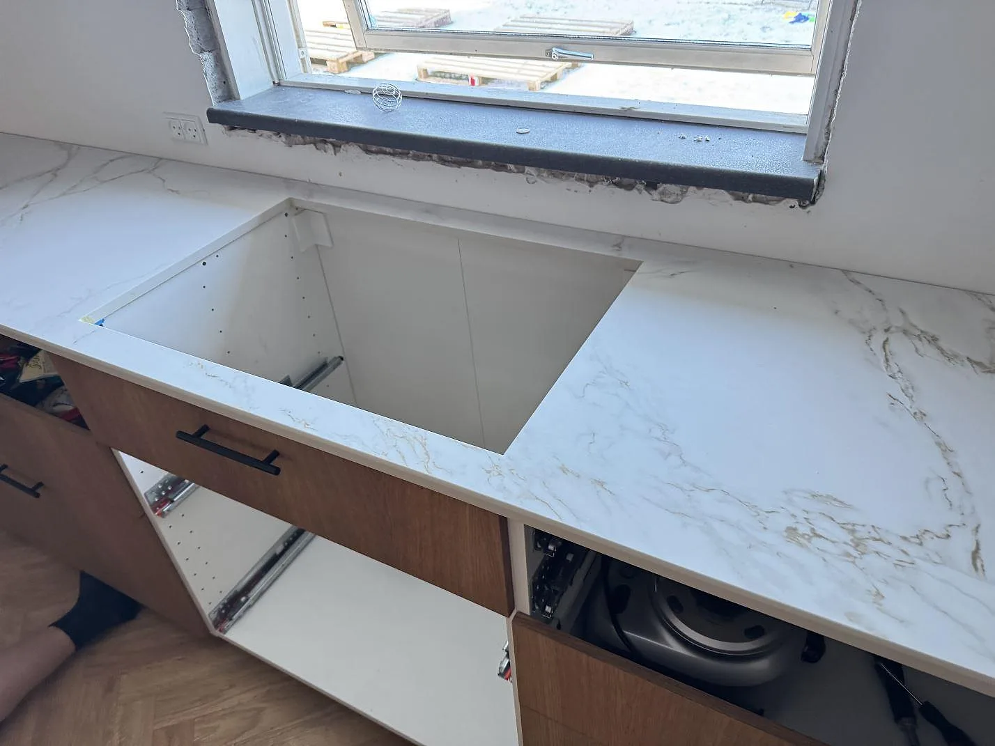 Köksbänkskiva i Dekton Entzo med urtag för häll över öppna stommar längs fönstret i ett kök under montering i Frederikssund.