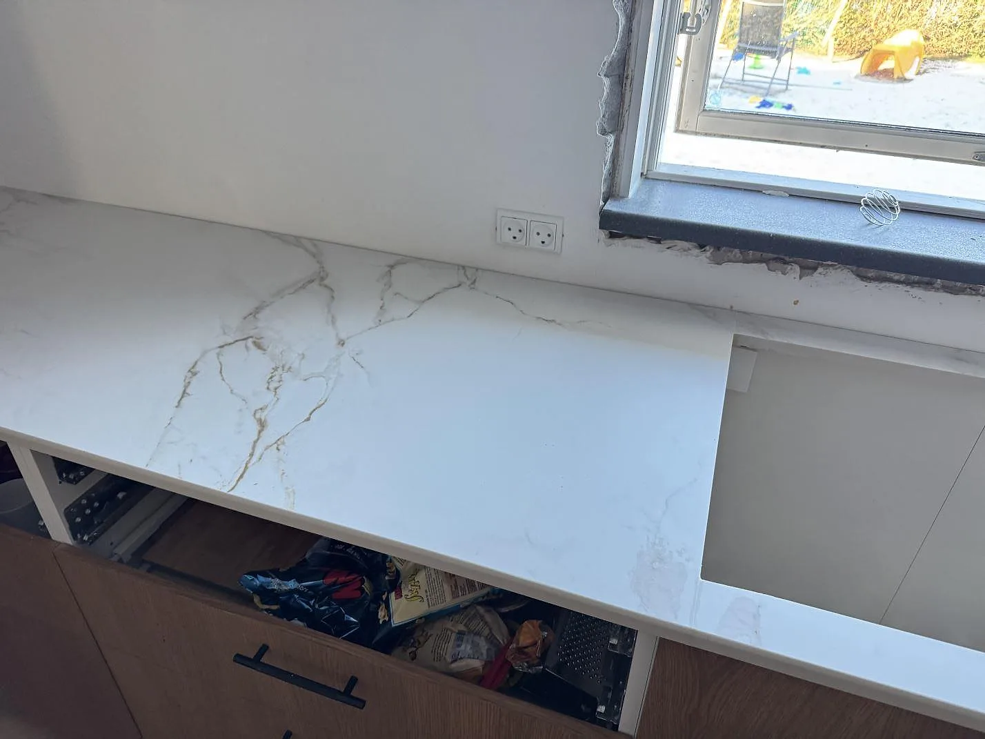 Lång köksbänk i ljus grått ådrad Dekton Entzo keramik med hällurtag och ekfronter i ett kök i Frederikssund.