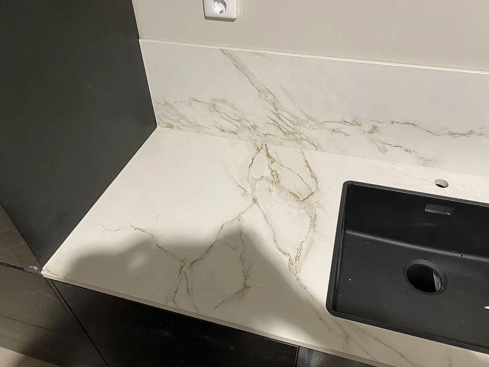 Hörn av Dekton Entzo köksbänkskiva i matt vit keramik med uppvikt stänkskydd och underlimmad svart kompositdiskho i ett kök i Göteborg.