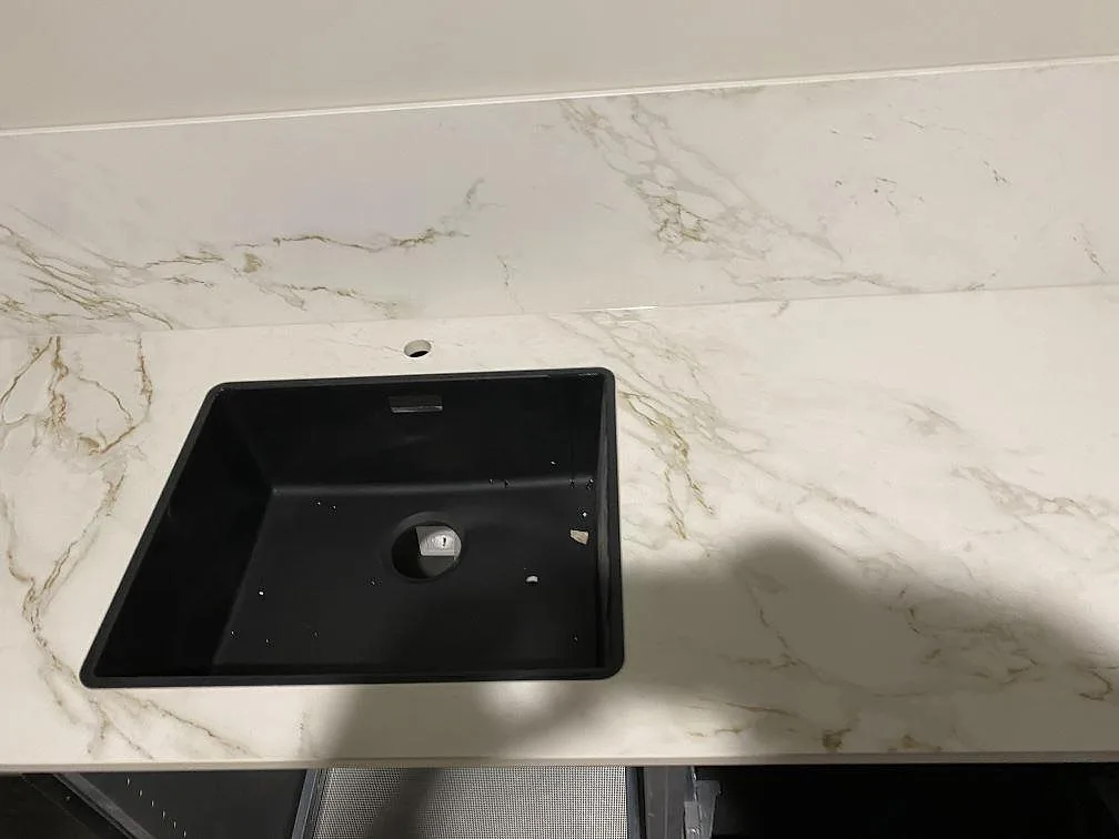 Underlimmad svart kompositdiskho infälld i matt vit Dekton Entzo köksbänkskiva med grågyllene ådring i ett kök i Göteborg.