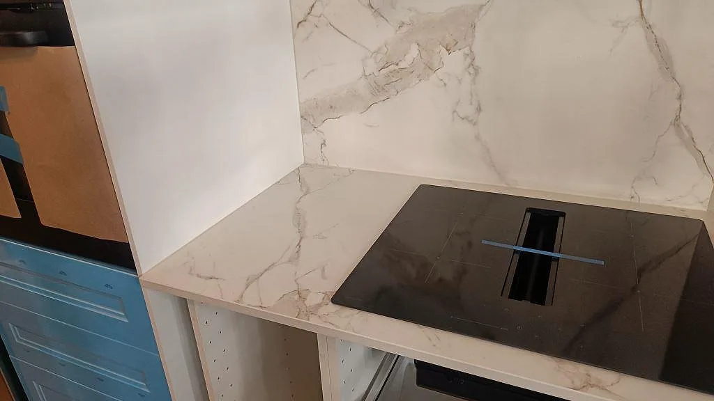 Vinklad vy över matt Dekton Entzo köksbänkskiva med svart induktionshäll och blå köksluckor i Göteborg.