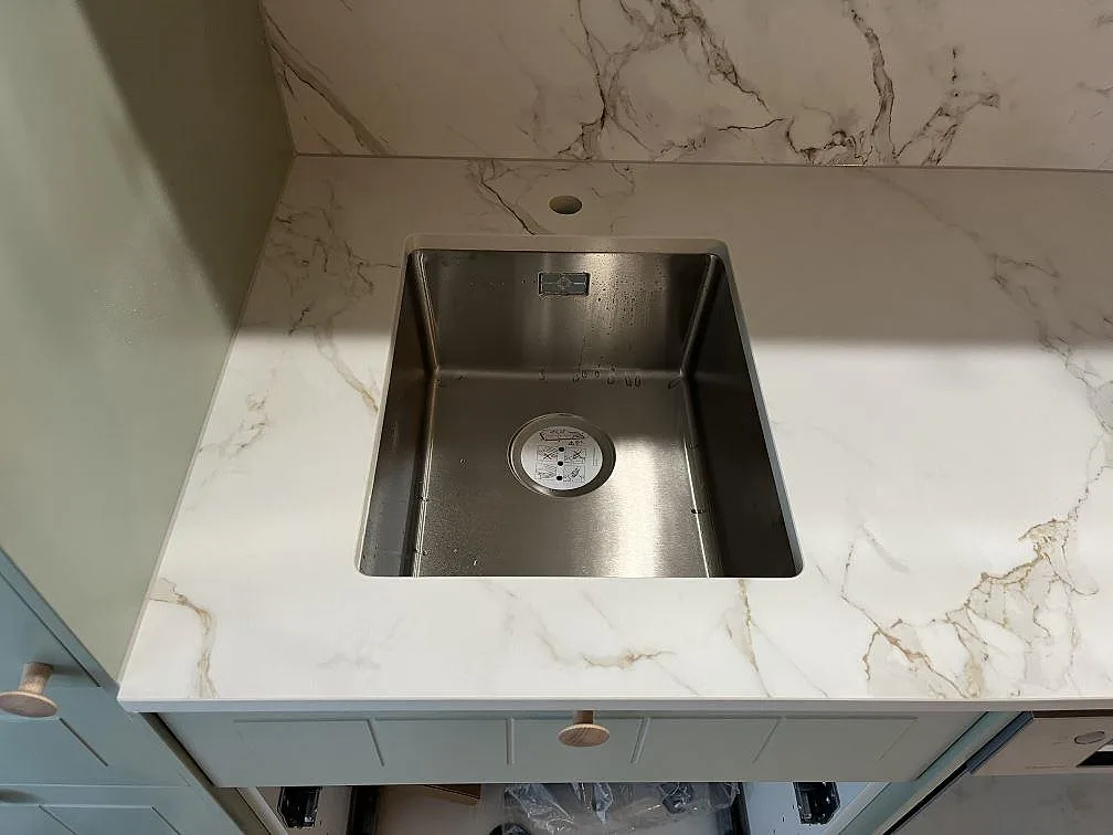 Underlimmad rostfri diskho infälld i köksbänkskiva av matt Dekton Entzo med vit ådrig yta i ett kök i Hägersten.
