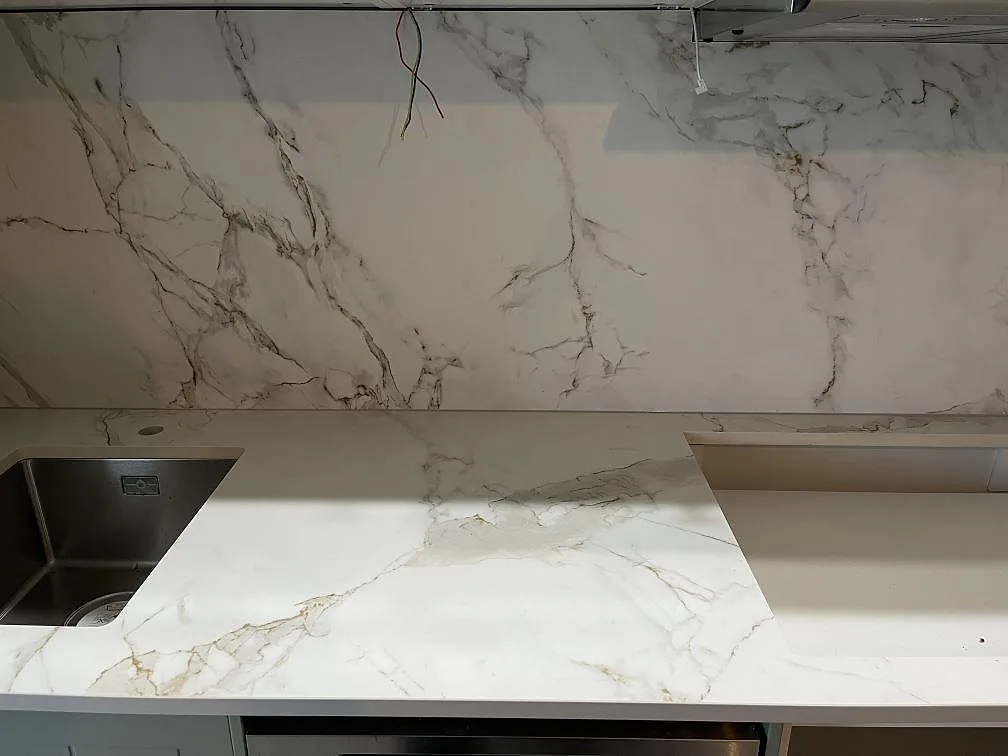 Vinkel över den raka köksbänken i matt Dekton Entzo i Hägersten med heltäckande stänkvägg i vit keramik och grå ådring under montering.