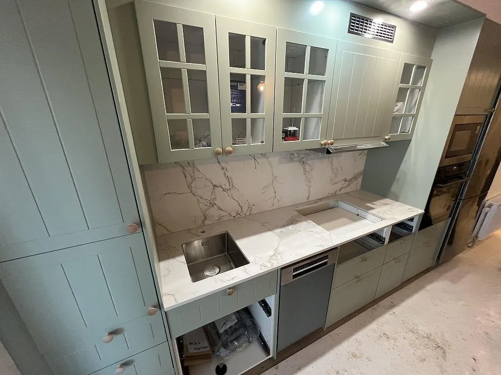 Köksbänkskiva i matt Dekton Entzo med vit Calacatta-lik yta och grå ådring i ett kök i Hägersten, med salviegröna shakerluckor, heltäckande stänkvägg i samma sten och underlimmad rostfri diskho.