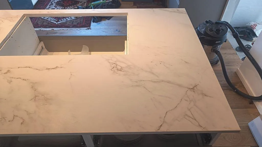 Ovanifrånsbild av matt Dekton Entzo på kökshalvö med stor öppning och ljus marmorerad keramik i Häljarp.