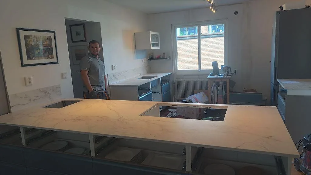Köksbänkskiva i matt Dekton Entzo, vit keramik med Calacatta-liknande ådring, på en stor halvö i ett kök i Häljarp.