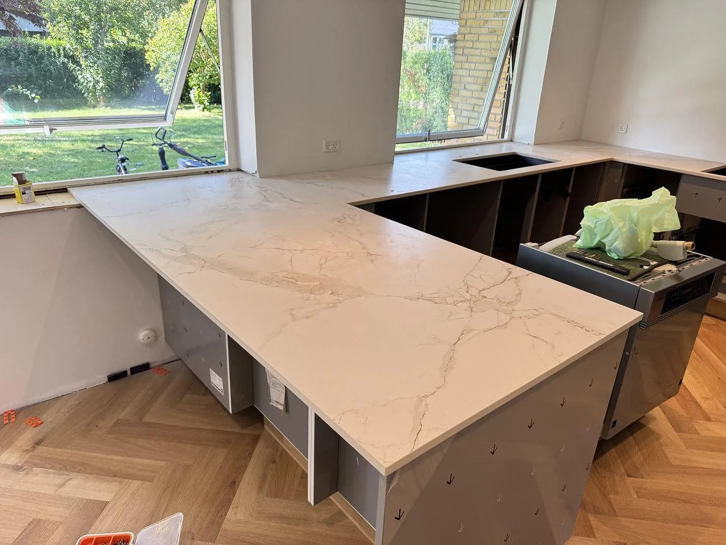 Köksbänkskiva i Dekton Entzo, 20 mm matt keramik, med ljus ådring, halvö och förberett hällurtag i ett kök under montering i Hedehusene.