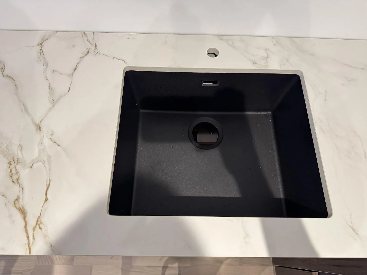Underlimmad svart kompositdiskho sett ovanifrån i en matt Dekton Entzo köksbänkskiva med kraftig ådring i ett kök i Hedehusene.