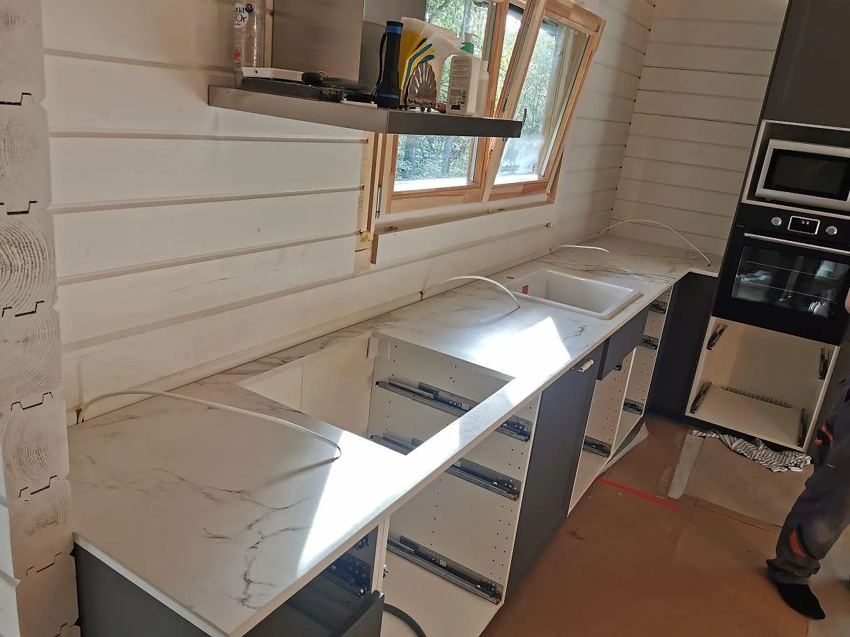 Köksbänkskiva i vit Dekton Entzo med marmorlik ådring och dubbel diskho under fönstret, monterad i ett kök i Hörby.