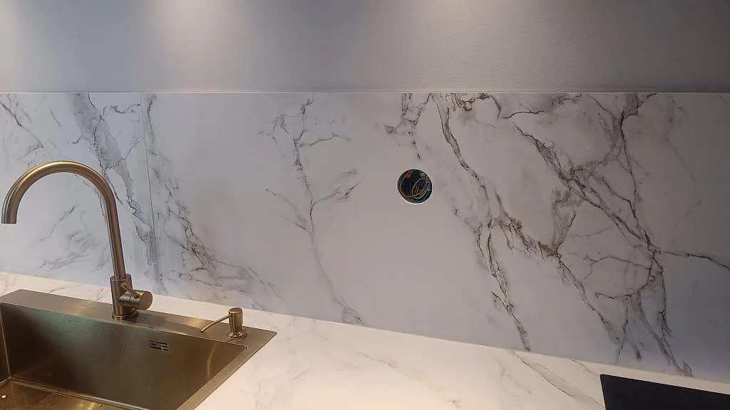 Närbild på matt Dekton Entzo kring diskho och mässingsfärgad blandare med marmorerat stänkskydd i ett kök i Jönköping.