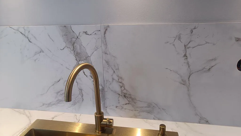 Närbild på mässingsfärgad köksblandare mot matt Dekton Entzo och marmorerad väggbeklädnad i Jönköping.