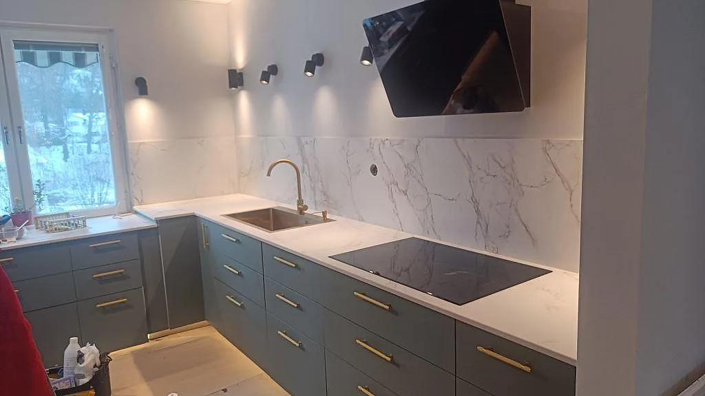 Köksbänkskiva i matt Dekton Entzo med grå luckor, mässingsdetaljer, induktionshäll och stänkskydd i Jönköping.